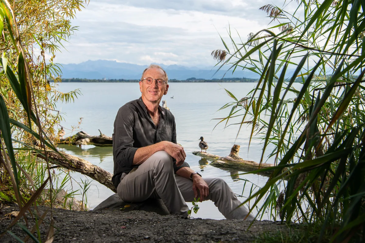 Hans-Michael Schmitt sitzt am Seeufer auf einem Baumstamm.